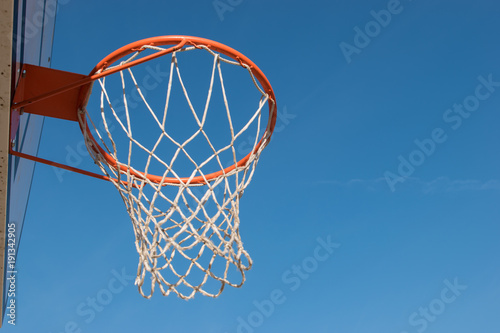 Closeup basketball hoop, basket with white net and blue sky in background © Domagoj