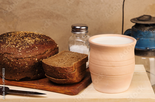 Rye bread with salt on a cutting board, clay pot with milk and a kerosene lantern. Still-life in the rustic style
