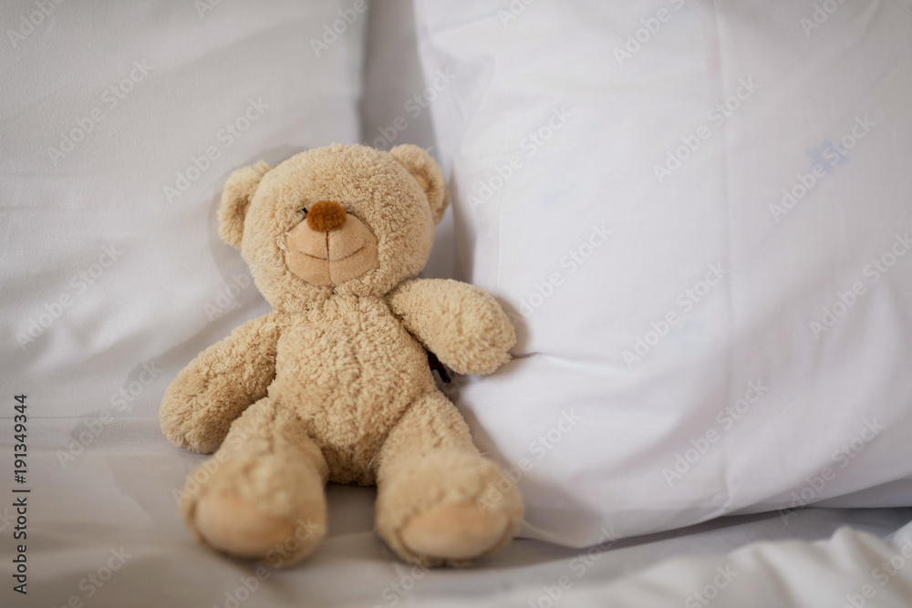 Sleeping teddy bear on white bed.