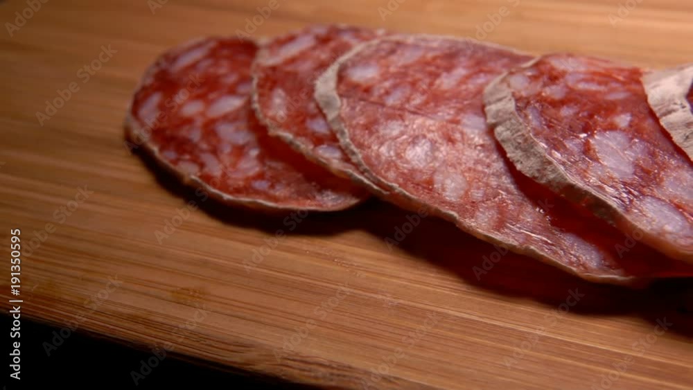 Fork takes a piece of uncooked jerked sausages in a natural shell from a wooden board Fork takes a piece of uncooked jerked sausages in a natural shell from a wooden board