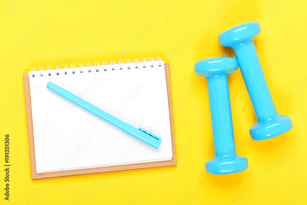 Notebook, pen and gym equipment top view on yellow background Notebook, pen and gym equipment top view on yellow background