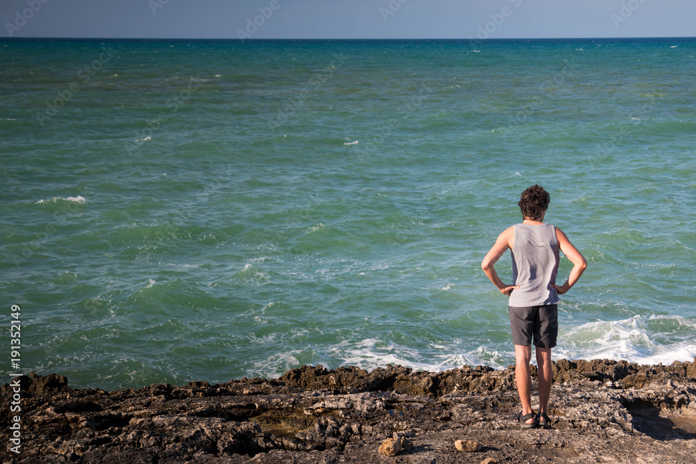 Landscape with blue sea and a young man on the beach. Background with copy space.