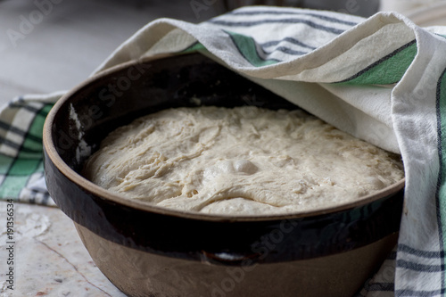 dough rising in large brown bowl covered with tea towel 