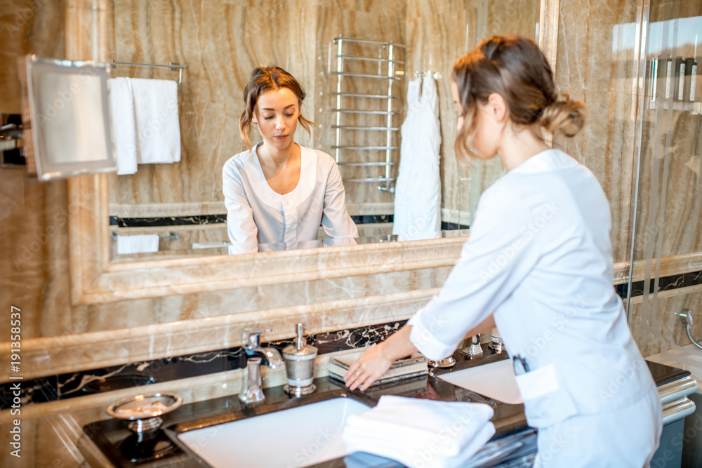 Fototapeta premium Young chambermaid in uniform cleaning a bathroom in the hotel