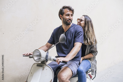 Loving couple riding an old scooter. The man is seated in front, while the woman is behind