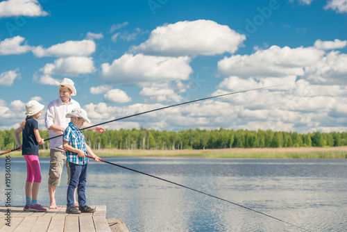 happy family on fishing - father, son and daughter with fishing rods on the pier