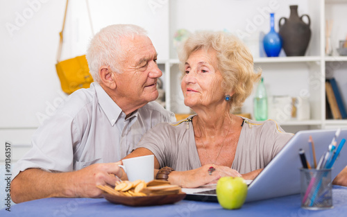 Smiling senior couple surfing net with laptop