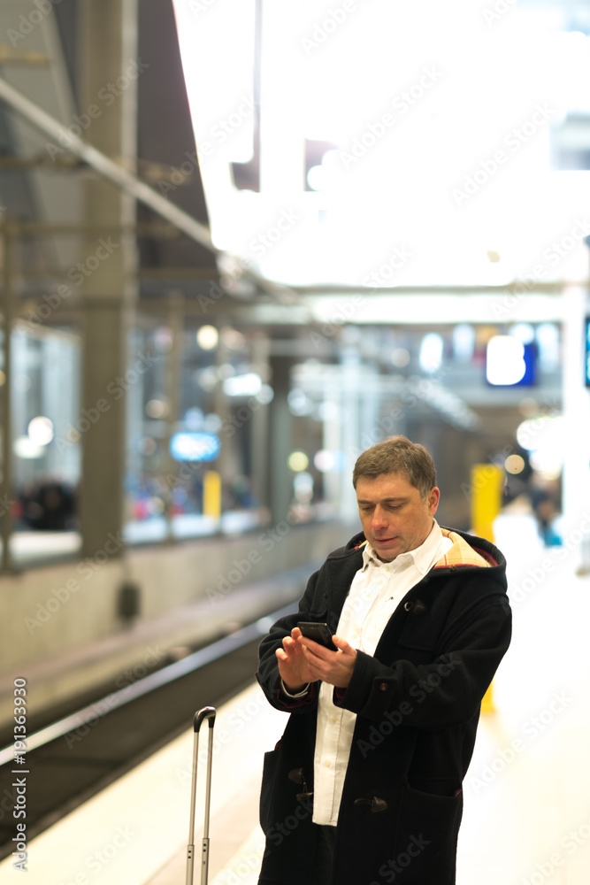 Businessman waiting for the train on railroad tracks checking his mobile phone Businessman waiting for the train on railroad tracks checking his mobile phone