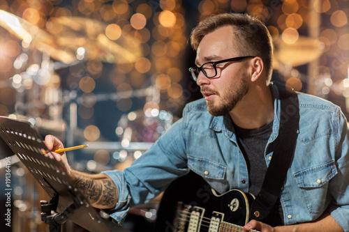 man with guitar writing to music book at studio photo