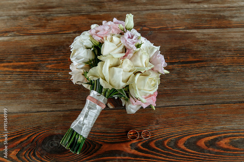 Wedding bouquet of cream and pink roses lies on a wooden surface. Wedding rings photo