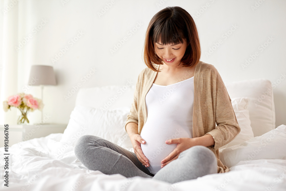 happy pregnant asian woman sitting in bed at home happy pregnant asian woman sitting in bed at home