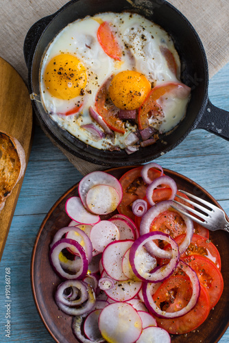 Fried eggs with tomatoes and spring salad with radishes and onions - rustic lunch