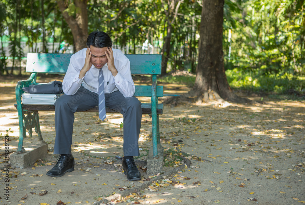 Stressed businessman holding his head sit on the bench in park,Concept worried about financial business