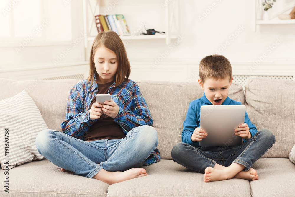 © Prostock-studio - Two kids with gadgets on couch at home
