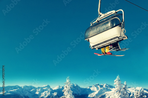people in chairlift at ski resort above snowy trees and mountains