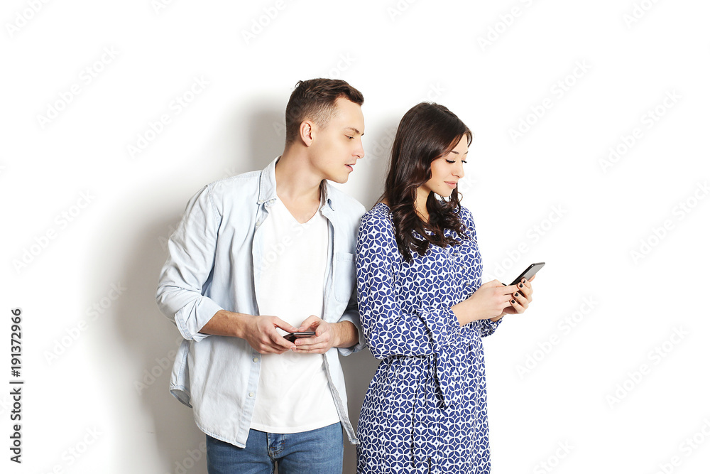 Jealous husband spying his wife mobile phone while she is reading a message. Technology & relationship concept. Modern romance troubles. Male and female online dating app. Swiping, browsing, surfing