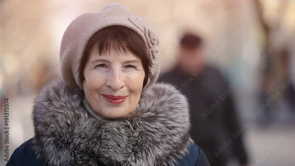 An optimistic view of a brunettte middle-aged woman in a fur coat and a knitted hat. She stands and smiles in a park alley on a sunny day in autumn. An optimistic view of a brunettte middle-aged woman in a fur coat and a knitted hat. She stands and smiles in a park alley on a sunny day in autumn.