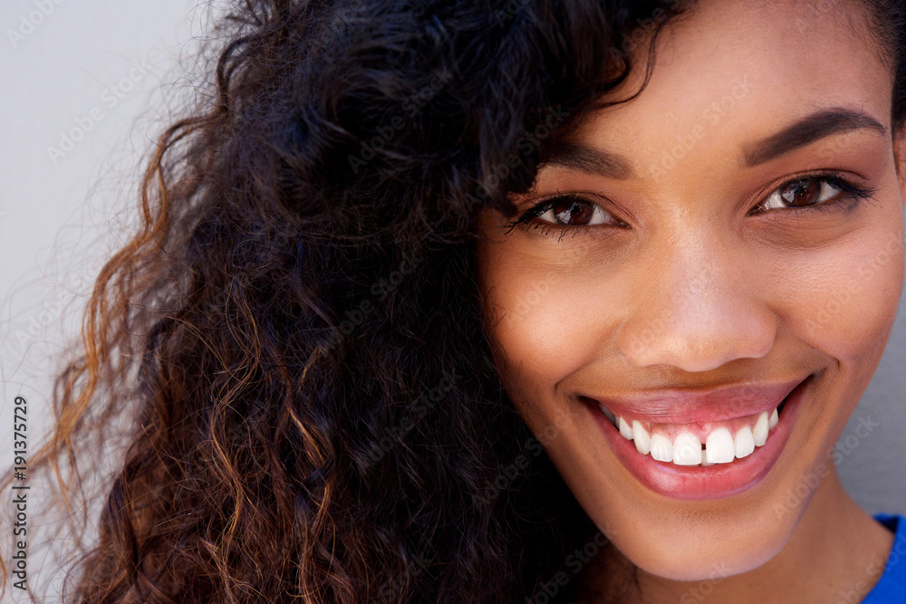 Close up beautiful young african american woman with curly hair smiling against gray backgorund Close up beautiful young african american woman with curly hair smiling against gray backgorund