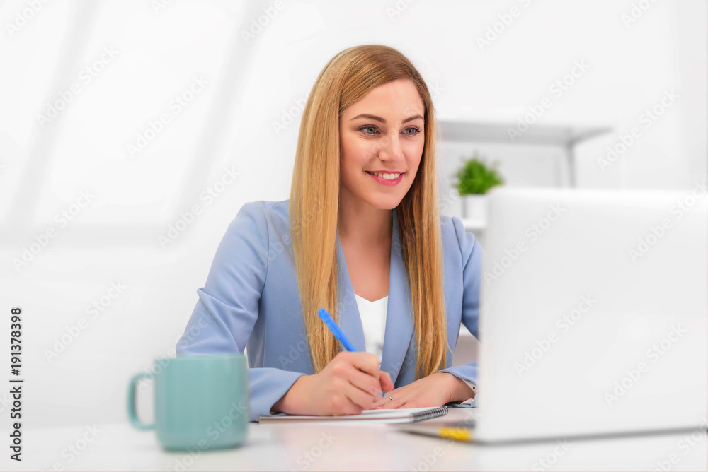 Beautiful young woman looks at the laptop monitor screen while sitting at the office desk. Beautiful young woman looks at the laptop monitor screen while sitting at the office desk.