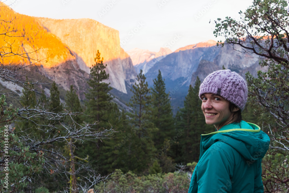 Young caucasian woman in winter clothing poses at sunset under half dome in Yosemite valley