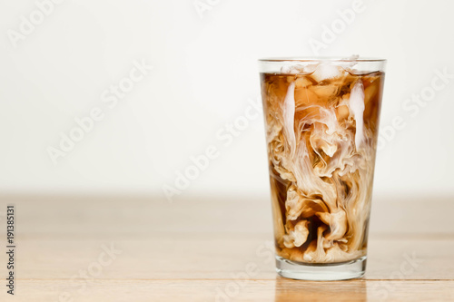 Print op canvas Iced coffee on a wood table with cream being poured into it showing the refreshi