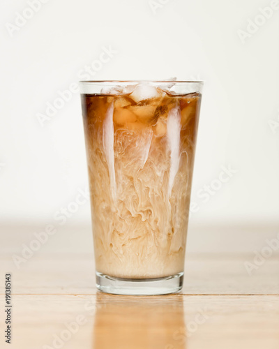 Iced coffee on a wood table with cream being poured into it showing the refreshing drink with a clean background