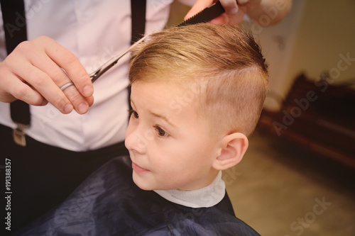 cute baby boy in a barber's chair in barbershop. Children's haircut.