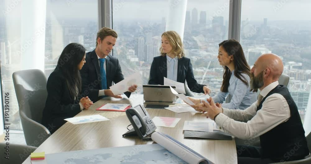 4k, Diverse team brainstorming and discussing business strategy across a boardroom table with London skyline in the background. Slow motion. 4k, Diverse team brainstorming and discussing business strategy across a boardroom table with London skyline in the background. Slow motion.