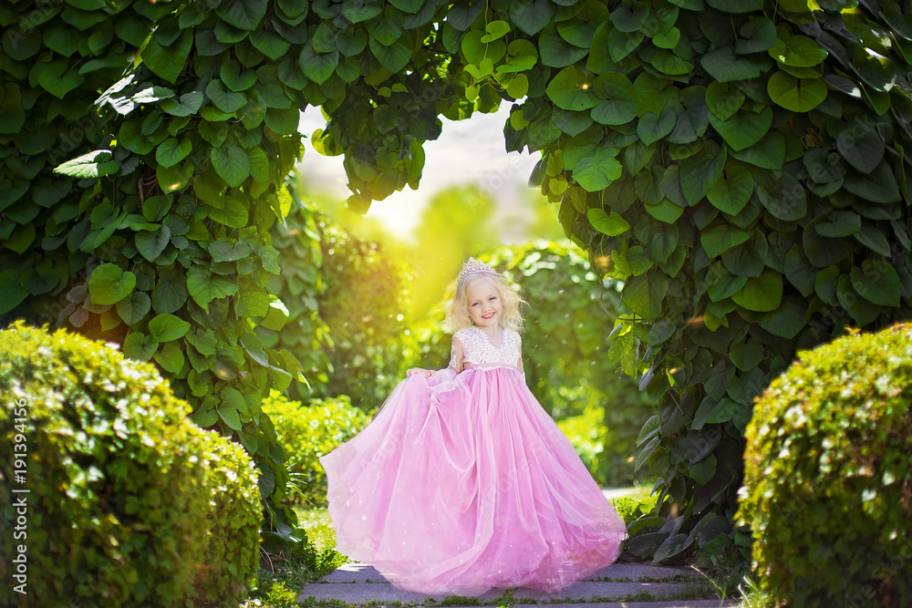 Beautiful little princess in pink dress on background of green arch in ...