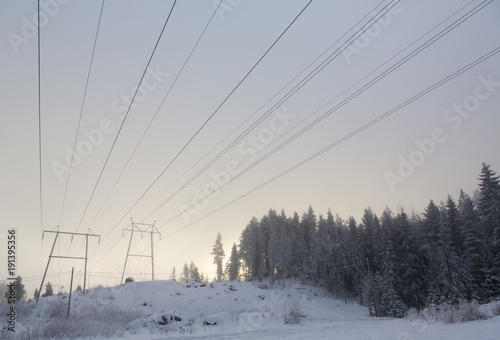 Power lines on a cold winter day. Sunset behind the forest. High usage of electricity due to cold climate.