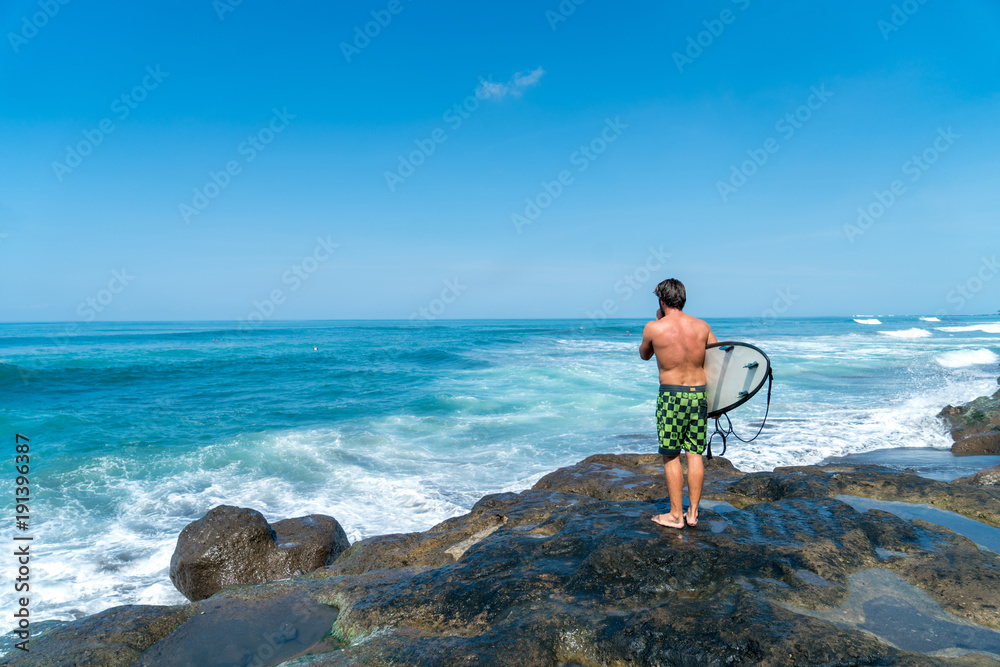 A surfer stands on the rocks