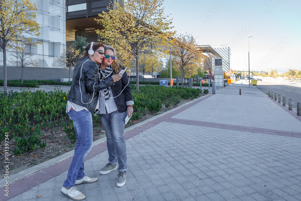 Two female friends listening to music on a street