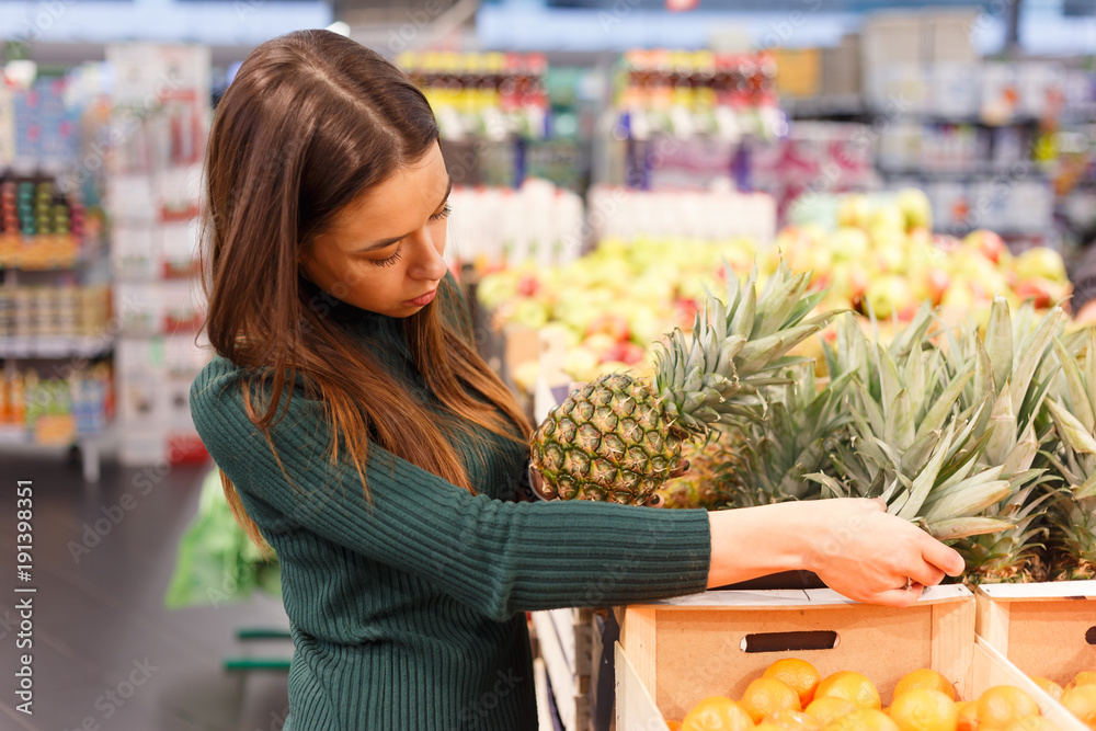Young brunette woman buying pineapple at grocery shop