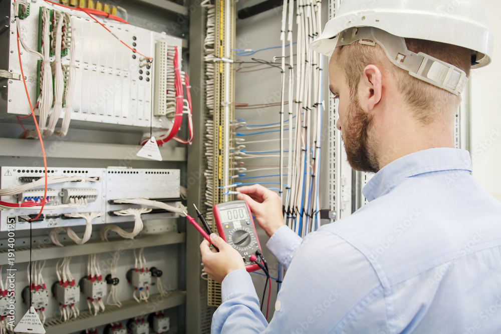 Fotografie Service man with multimeter in hands adjusts electric control panel