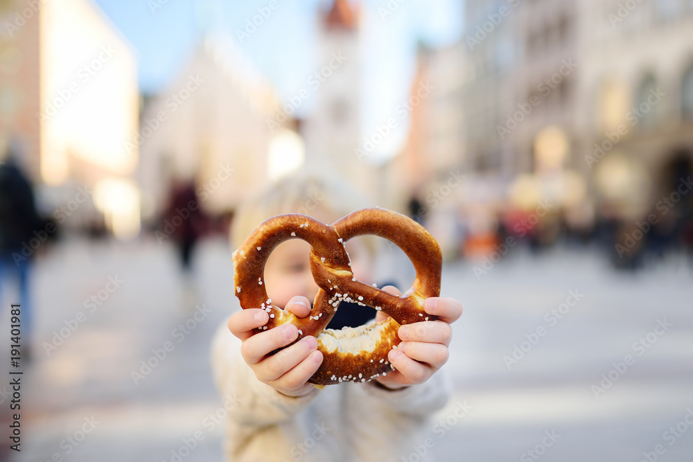 Fototapeta premium Little tourist holding traditional bavarian pretzel in Munich
