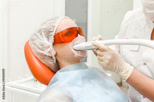 Obraz na plátně Woman patient in dental clinic whitening her teeth with UV lamp, stomatology and