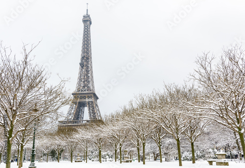 Fototapeta Naklejka Na Ścianę i Meble -  Winter in Paris in the snow. The Eiffel tower seen from the Champ de Mars with a snow covered tree lined alley in the foreground.