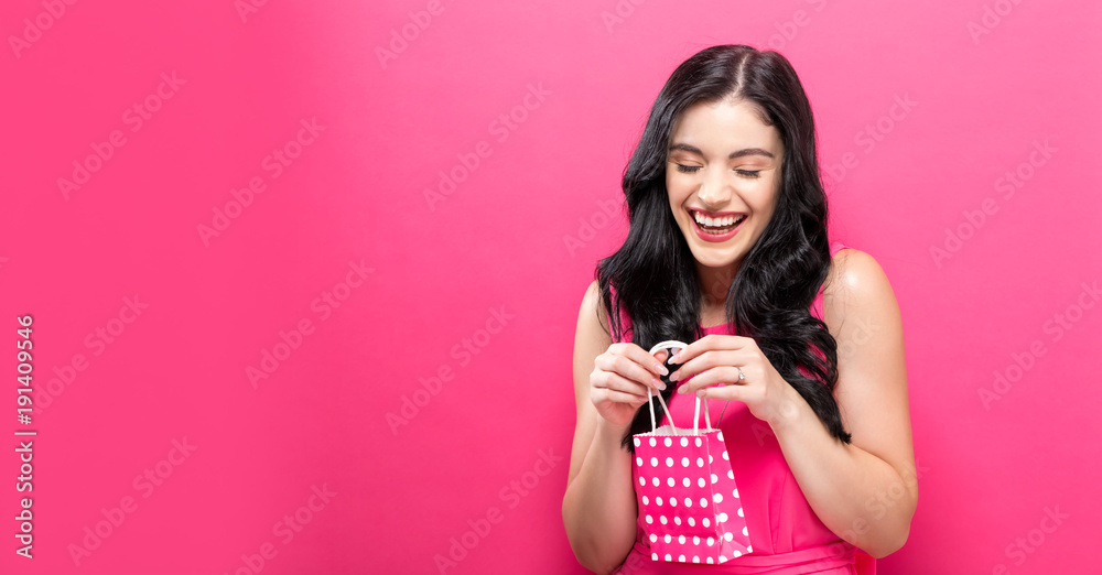 Young woman holding a tiny shopping bag on a pink background Young woman holding a tiny shopping bag on a pink background