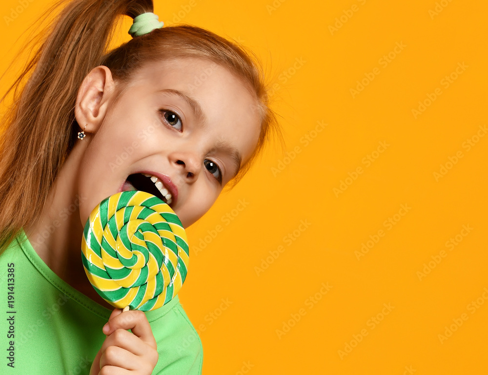 Happy young little child girl kid bite sweet lollypop candy
