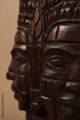 Closeup of a wooden mask sculpture from Cambodia  showing two faces looking perpendicular to each other with the front facing carving in focus.