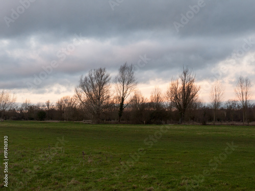 sunset moody sky winter autumn over green field with trees water © Callum