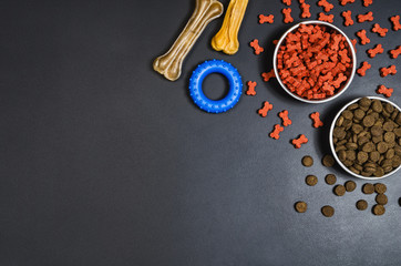 Dry dog pet food in bowl and accessories on blach chalkboard background top view. Pet feeding concept backgrounds with copy space. Photograph taken from above.
