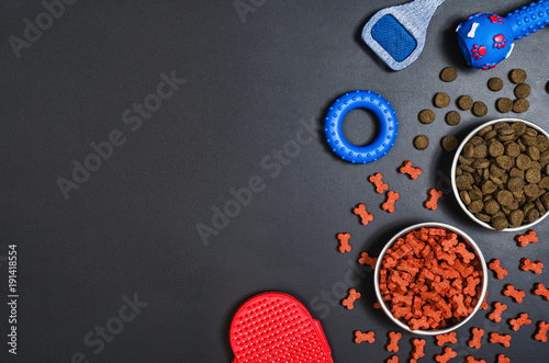 Dry dog pet food in bowl and accessories on blach chalkboard background top view. Pet feeding concept backgrounds with copy space. Photograph taken from above.