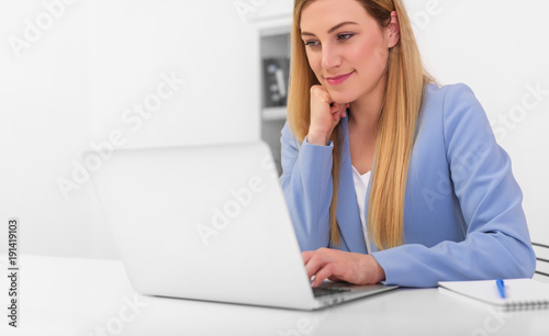 Beautiful young woman looks at the laptop monitor screen while sitting at the office desk.