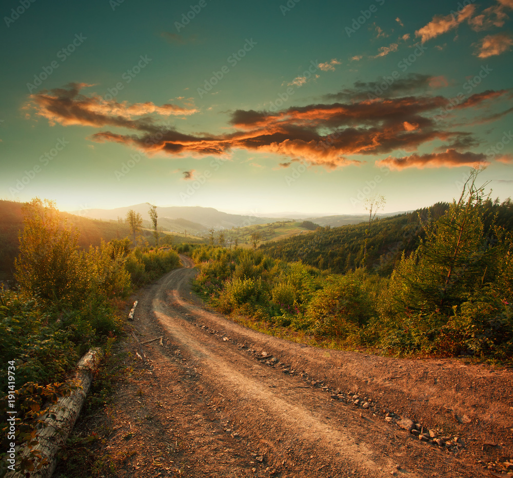 Dirt road in mountains at sunset dramatic sky background