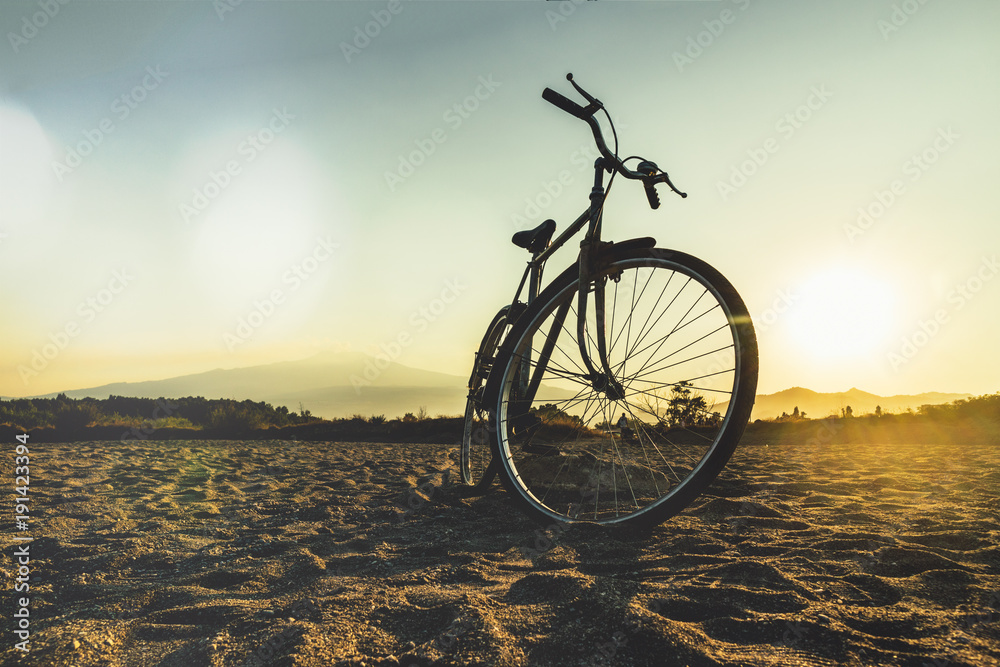 Silhouette of an ancient backlit bicycle parked on the beach at the foot of the Etna volcano Silhouette of an ancient backlit bicycle parked on the beach at the foot of the Etna volcano