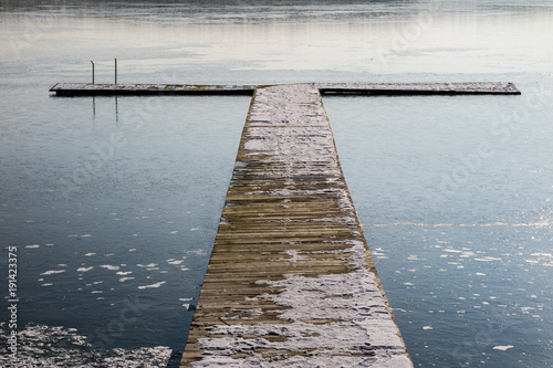 Fishing pier on a frozen lake. Bridge for mooring fishing boats and ice on the lake.