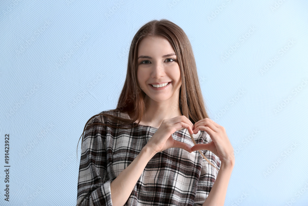 Portrait of beautiful smiling woman making heart with her hands on light background Portrait of beautiful smiling woman making heart with her hands on light background