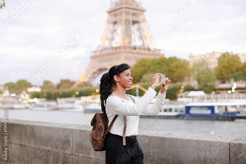 Canvas Print Lady standing on embankment not far from Eiffel Tower in Paris and watching pictures of landmarks made during day on mobile