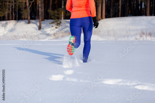 Close-up of a young woman in bright purple leggings and sneakers running through the winter snow on a bright winter day, rear view. Following from a sneaker in the snow photo